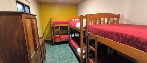 A dormitory room with bunk beds, a wooden wardrobe, and a green carpet.