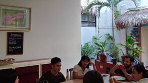 A group of people seated around a table in a room with a ceiling fan, a chalkboard menu, and potted plants. - Flying Dog Hostels Iquitos (Iquitos)