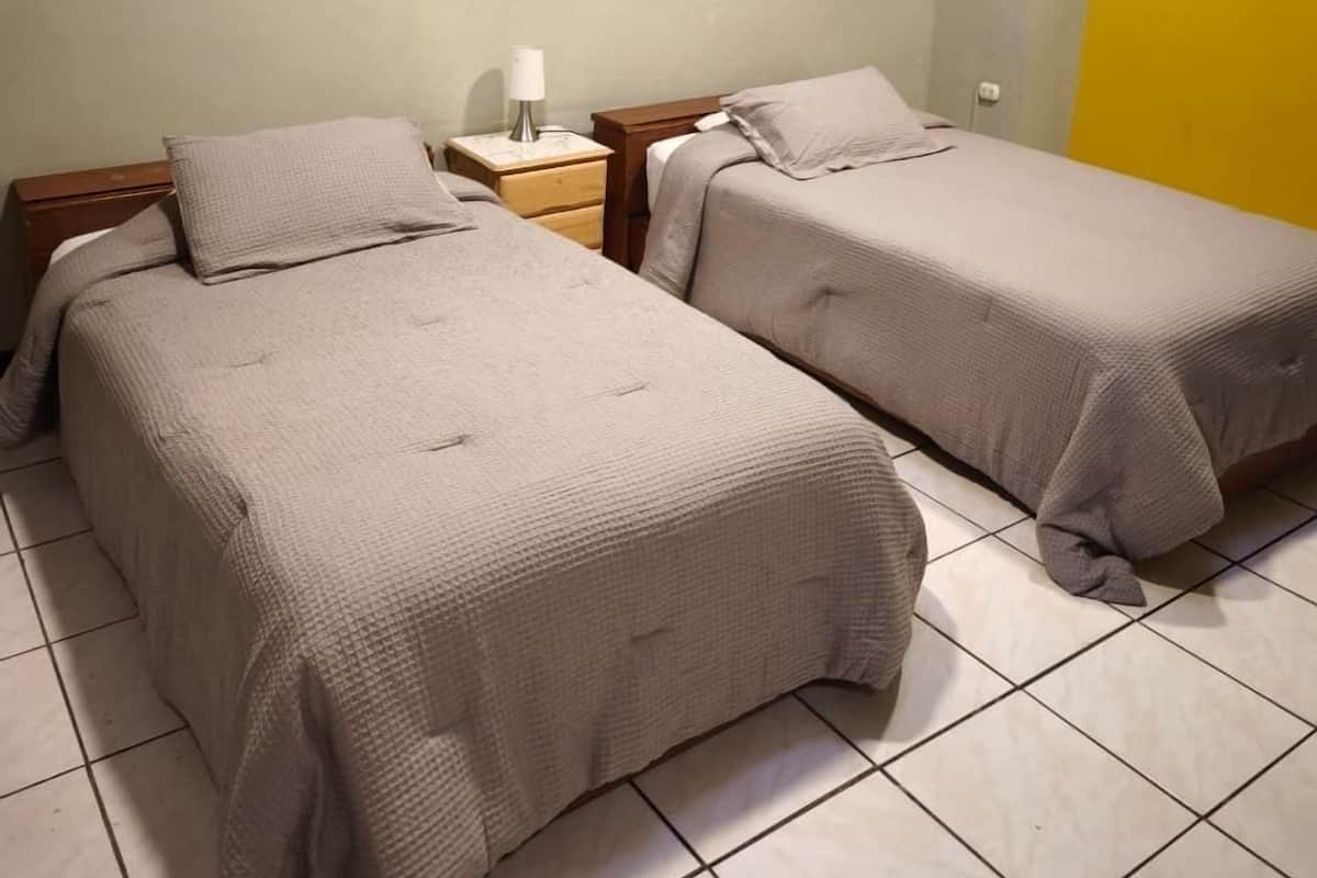 A hotel room with two beds, a nightstand, a lamp, and two framed pictures on the wall.