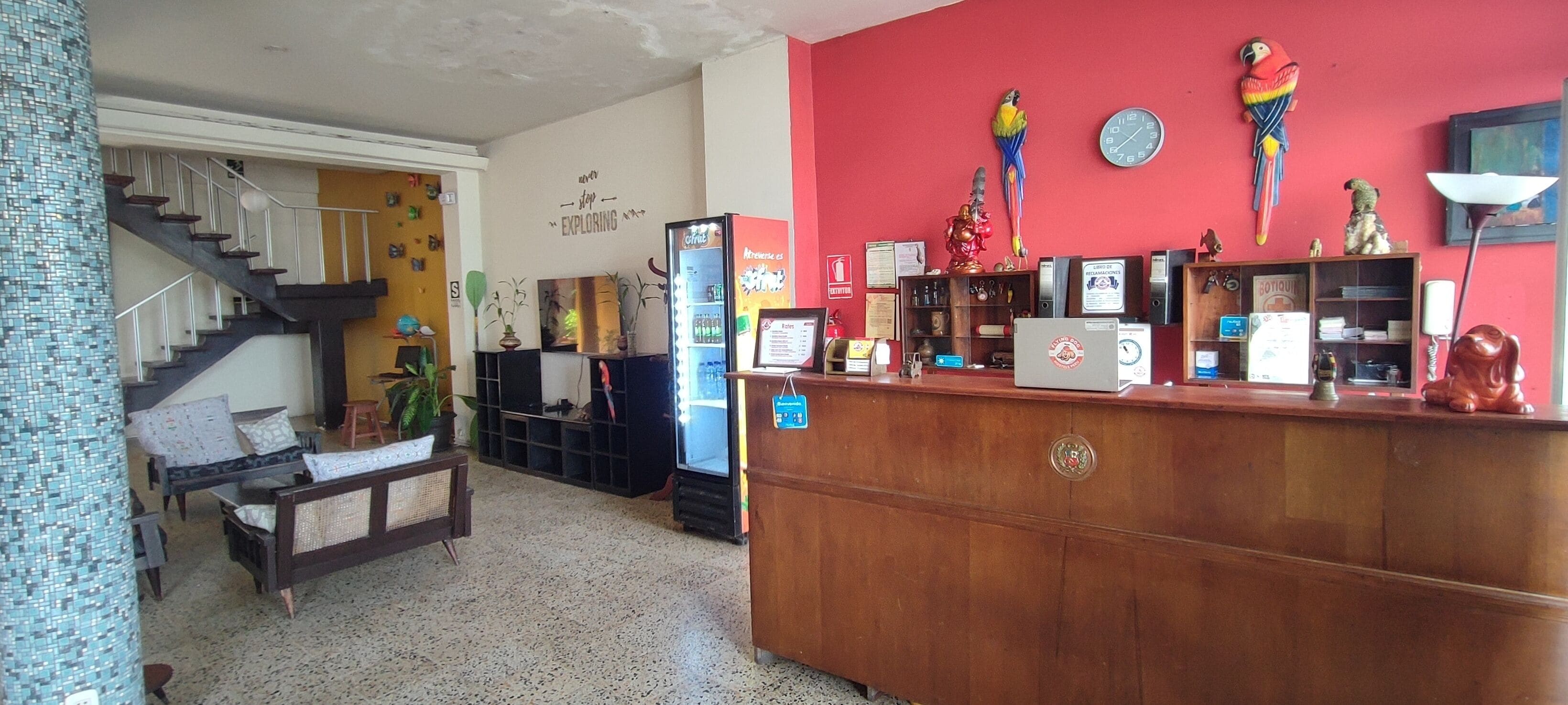 A reception area with a wooden desk, a refrigerator, a clock, and a staircase leading to another floor.
