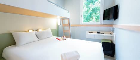 Habitación de hotel con cama, televisor montado en la pared, ventana con vista a zonas verdes y un escritorio pequeño con una silla.