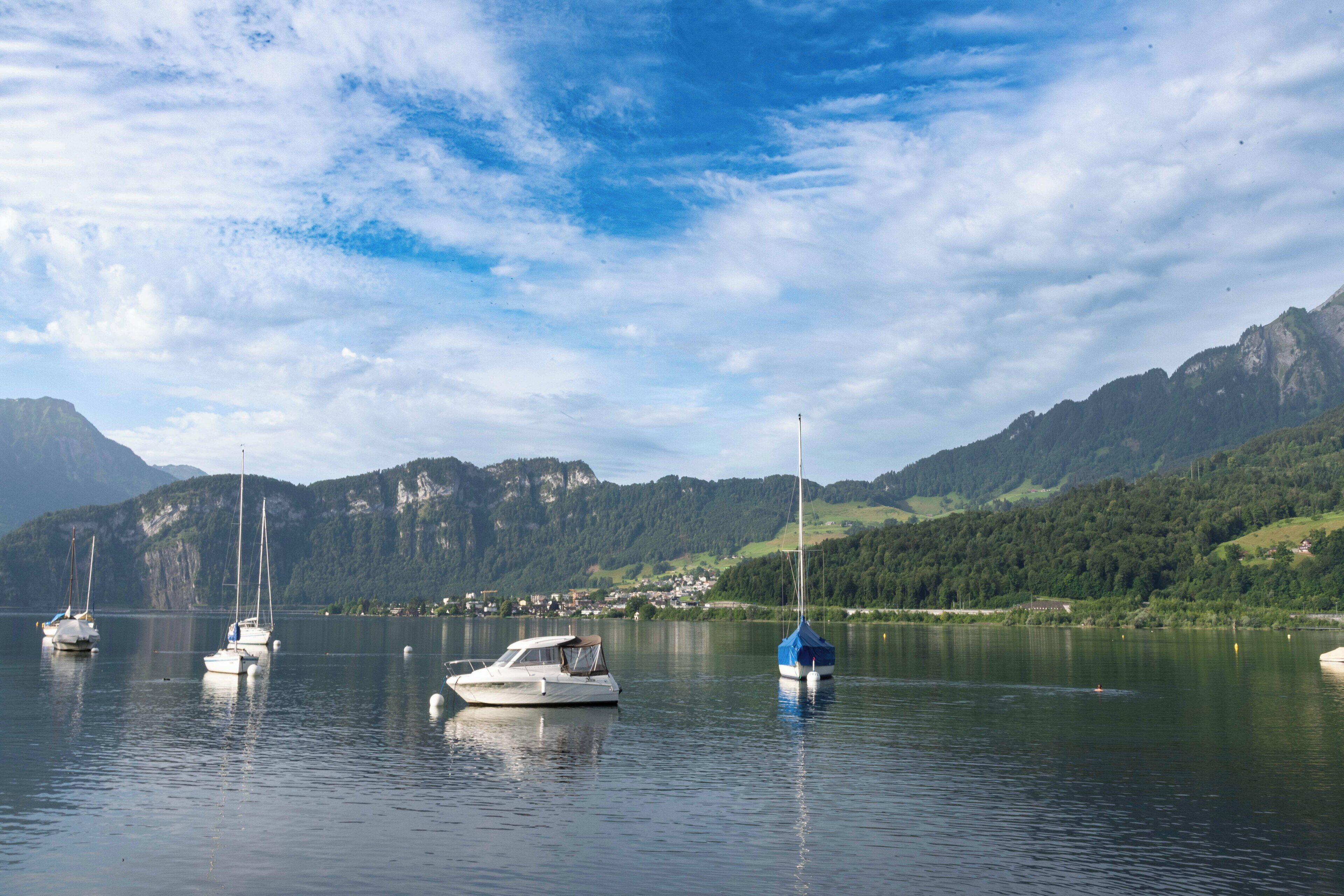 A calm lake with several boats anchored, surrounded by mountains and a clear sky.