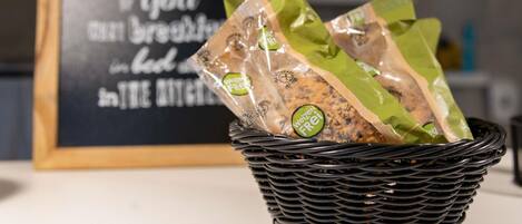 Una cesta negra tejida, llena de alimentos envasados en verde y marrón, sobre una mesa.