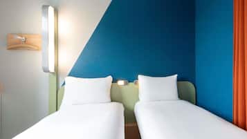 Habitación de hotel con dos camas individuales, una mesita de noche, una lámpara de pared y un perchero de madera.