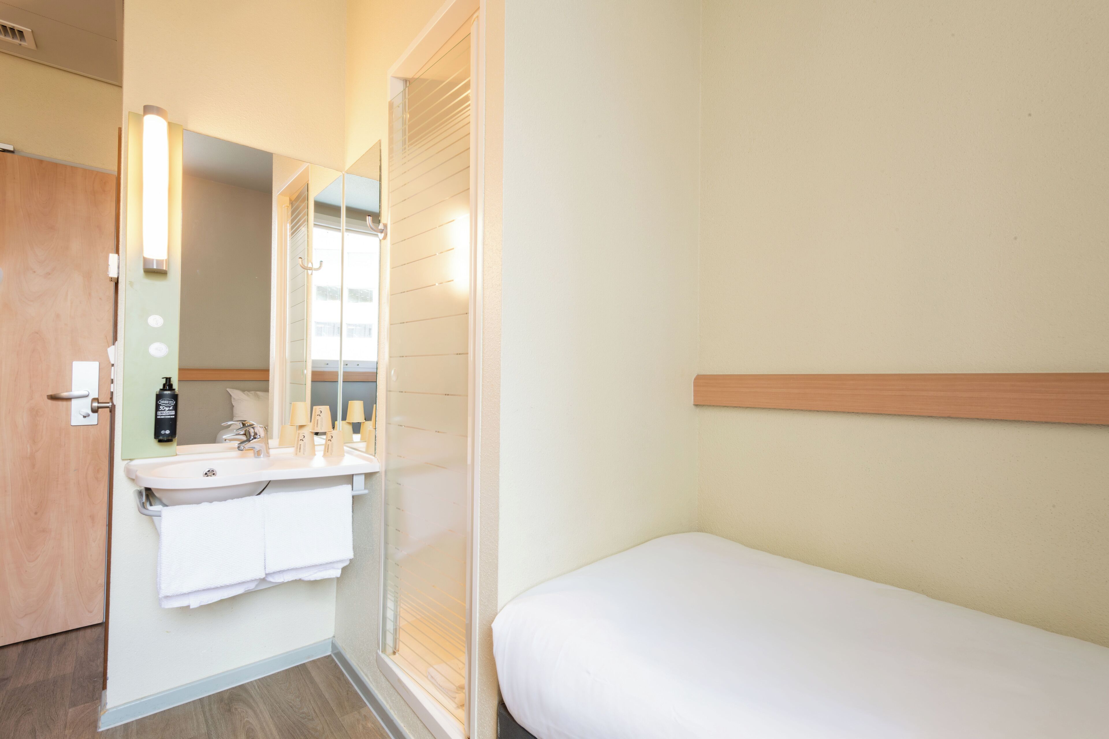 A hotel room with a bathroom, a bed, and a mirror.