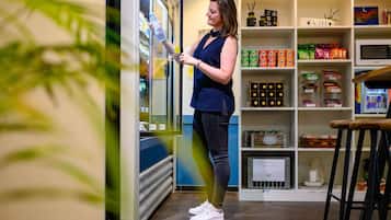 A woman standing in front of a refrigerator in a bar area, with shelves stocked with snacks and a sign that reads "BAR" above.