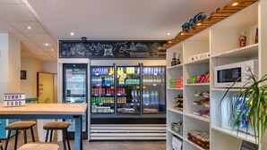 Un café moderno con área de bar, asientos, un refrigerador lleno de bebidas y estantes con bocadillos.