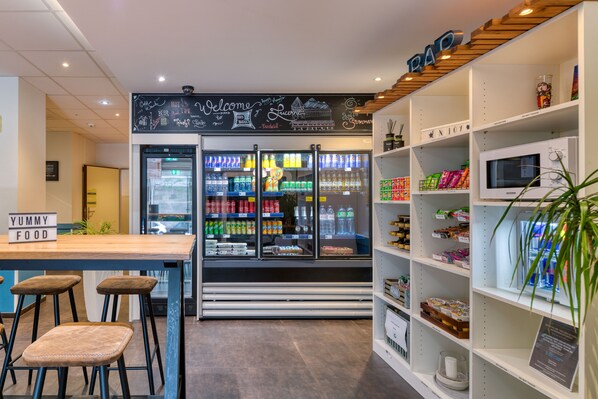 Ein modernes Café-Interieur mit Barbereich, Sitzgelegenheiten, einem mit Getränken gefüllten Kühlschrank und Regalen voller Snacks.