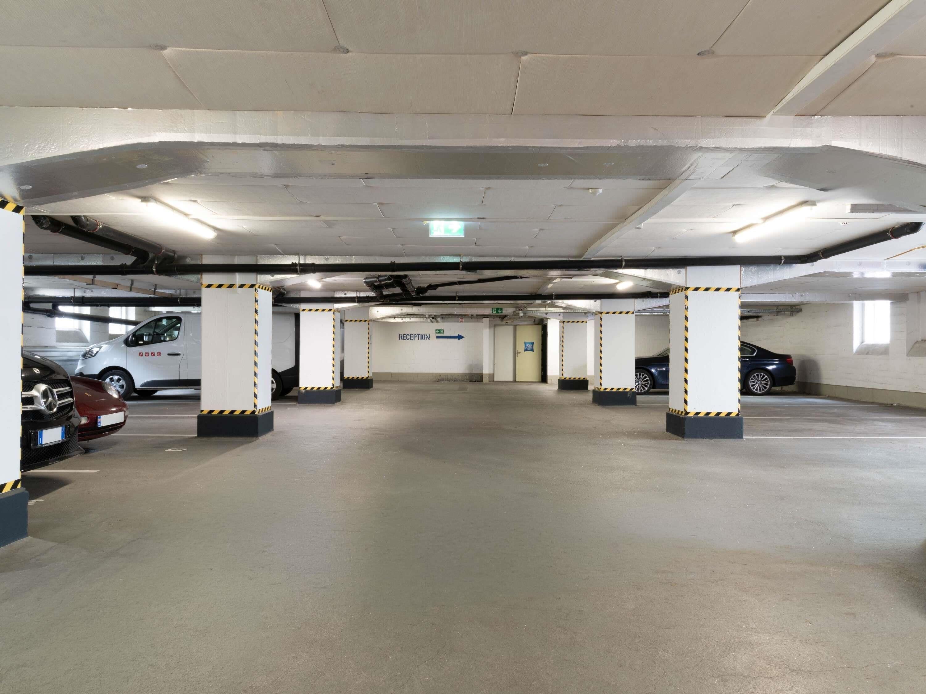 Un parking à plusieurs niveaux avec plusieurs voitures stationnées, des piliers en béton et un espace d’accueil.