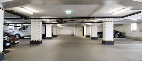 Un parking à plusieurs niveaux avec plusieurs voitures stationnées, des piliers en béton et un espace d’accueil.
