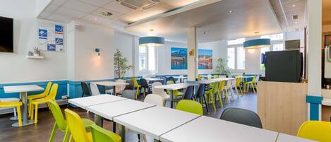 A modern dining area with white tables and colorful chairs, large windows, and ceiling vents.