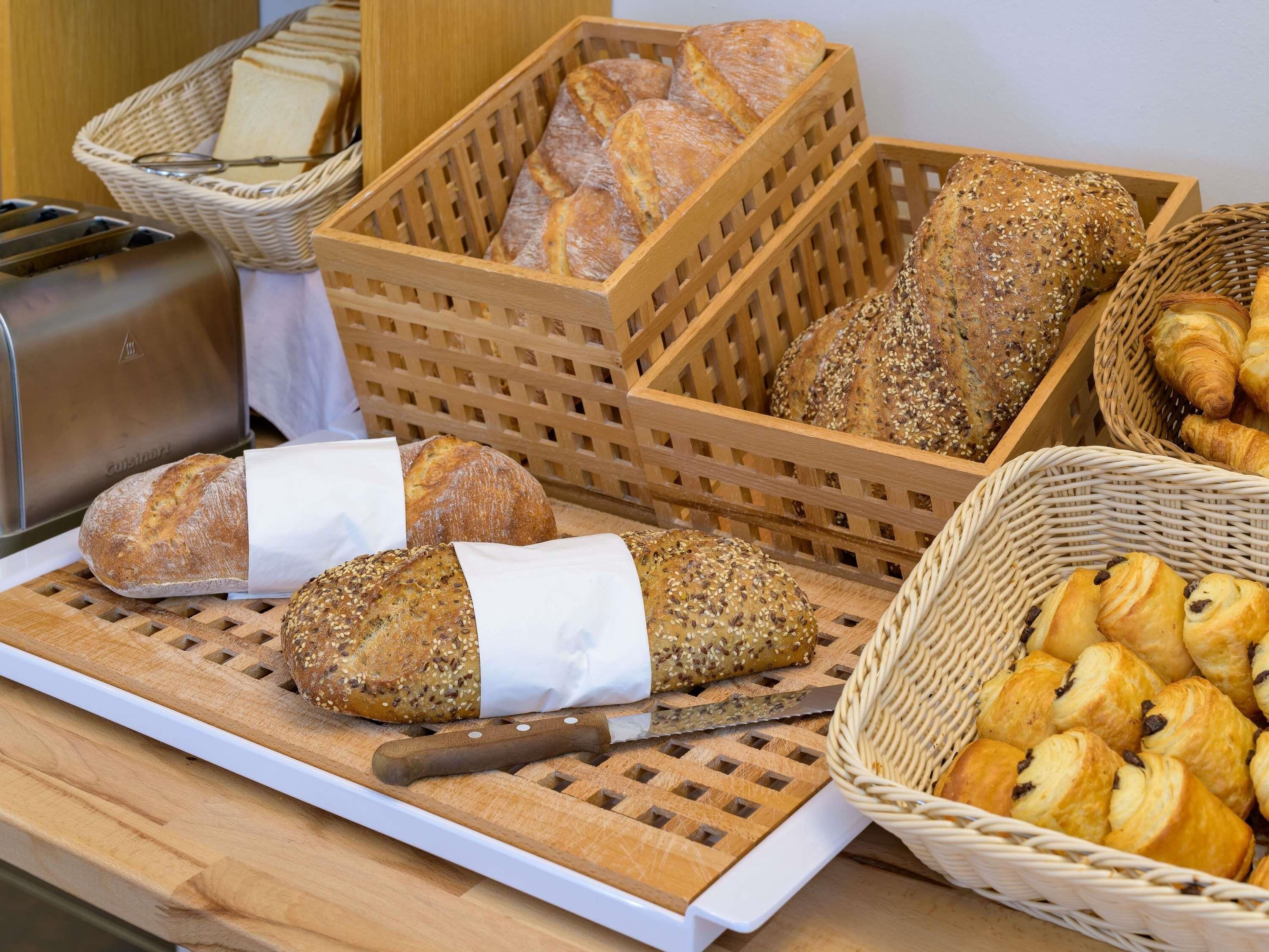 Une variété de pains et de viennoiseries sont disposés sur une table en bois, notamment des pains, des croissants et un panier de biscuits.