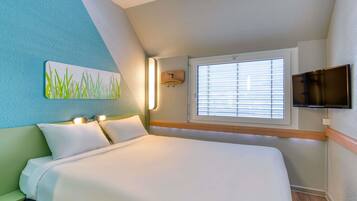 Habitación de hotel con cama, un cuadro de hierba, ventana con persianas y televisor montado en la pared.