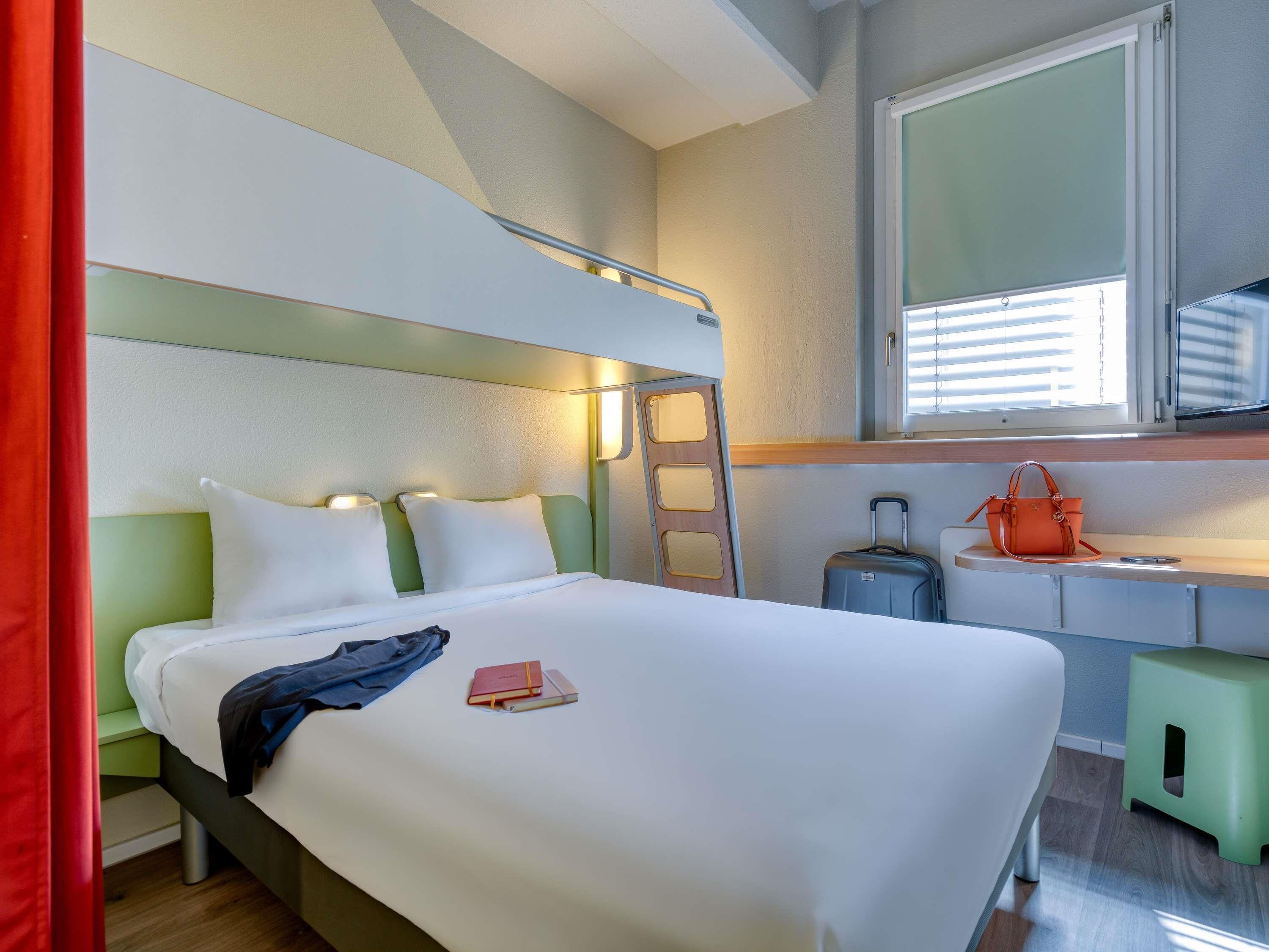 A hotel room with a bed, a suitcase, a handbag, a ladder, and a window with blinds.