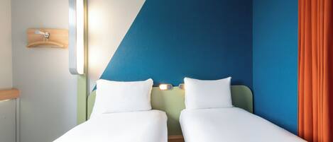 A hotel room with two single beds, a nightstand, a wall-mounted lamp, and a curtain.