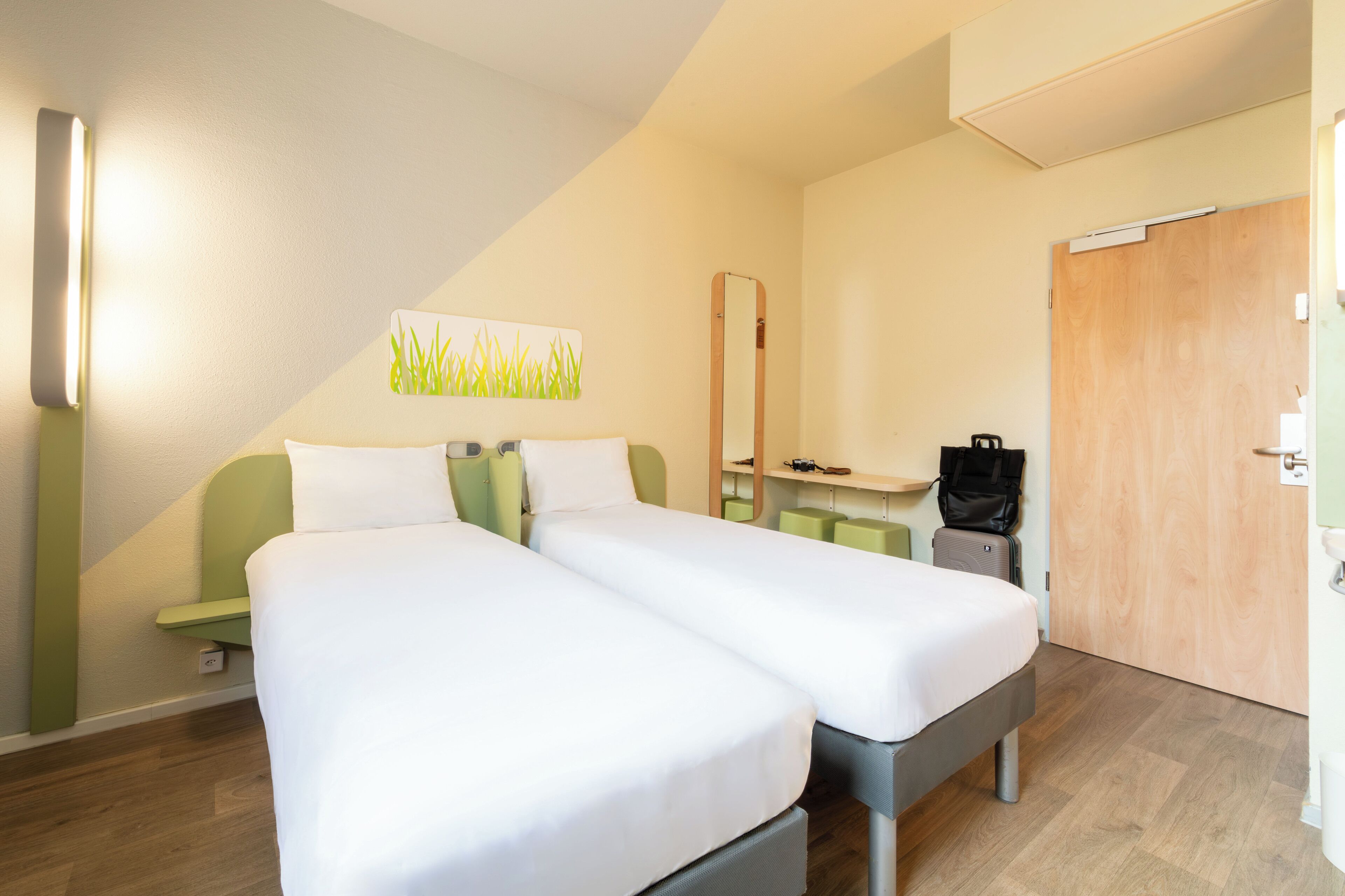 Habitación de hotel con dos camas individuales, un escritorio pequeño, un espejo y una puerta.
