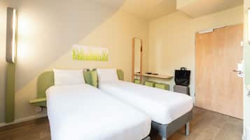 Habitación de hotel con dos camas individuales, un escritorio pequeño, un espejo y una puerta.