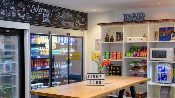 Una zona de bar con una mesa de madera, taburetes y estantes llenos de aperitivos y bebidas.