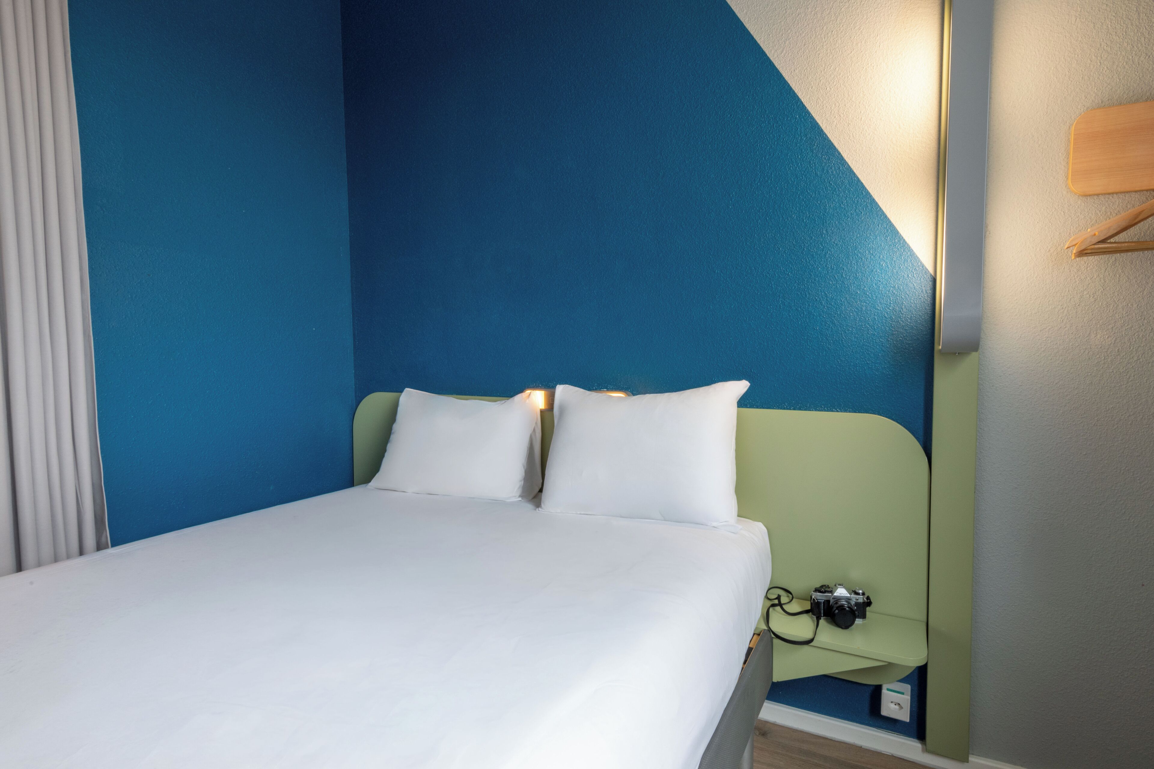 Una habitación de hotel con cama, almohadas, una mesita de noche y una cámara sobre ella.