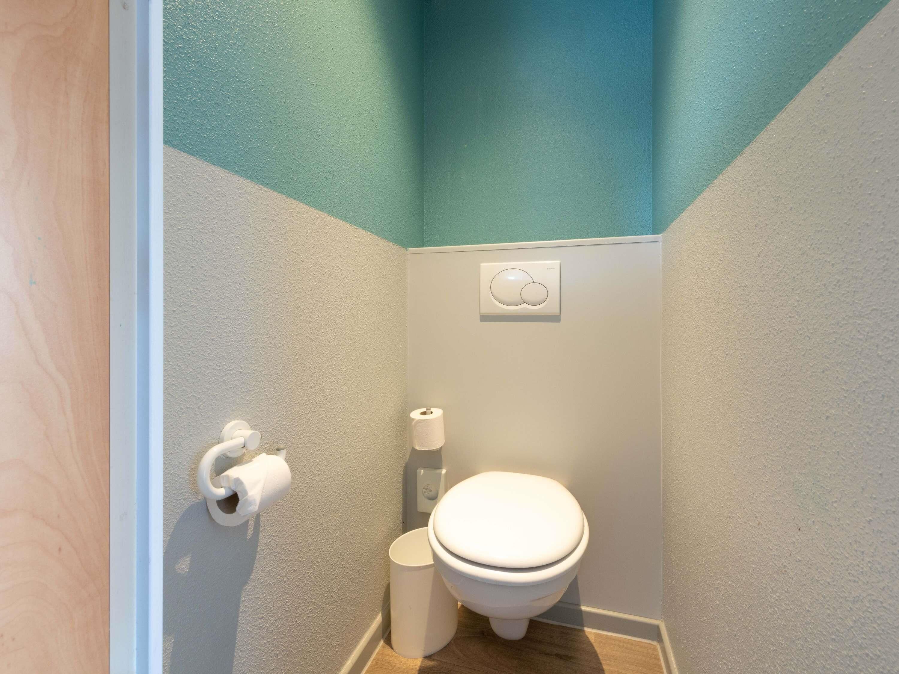 A small bathroom with a toilet, toilet paper, and a hand dryer.
