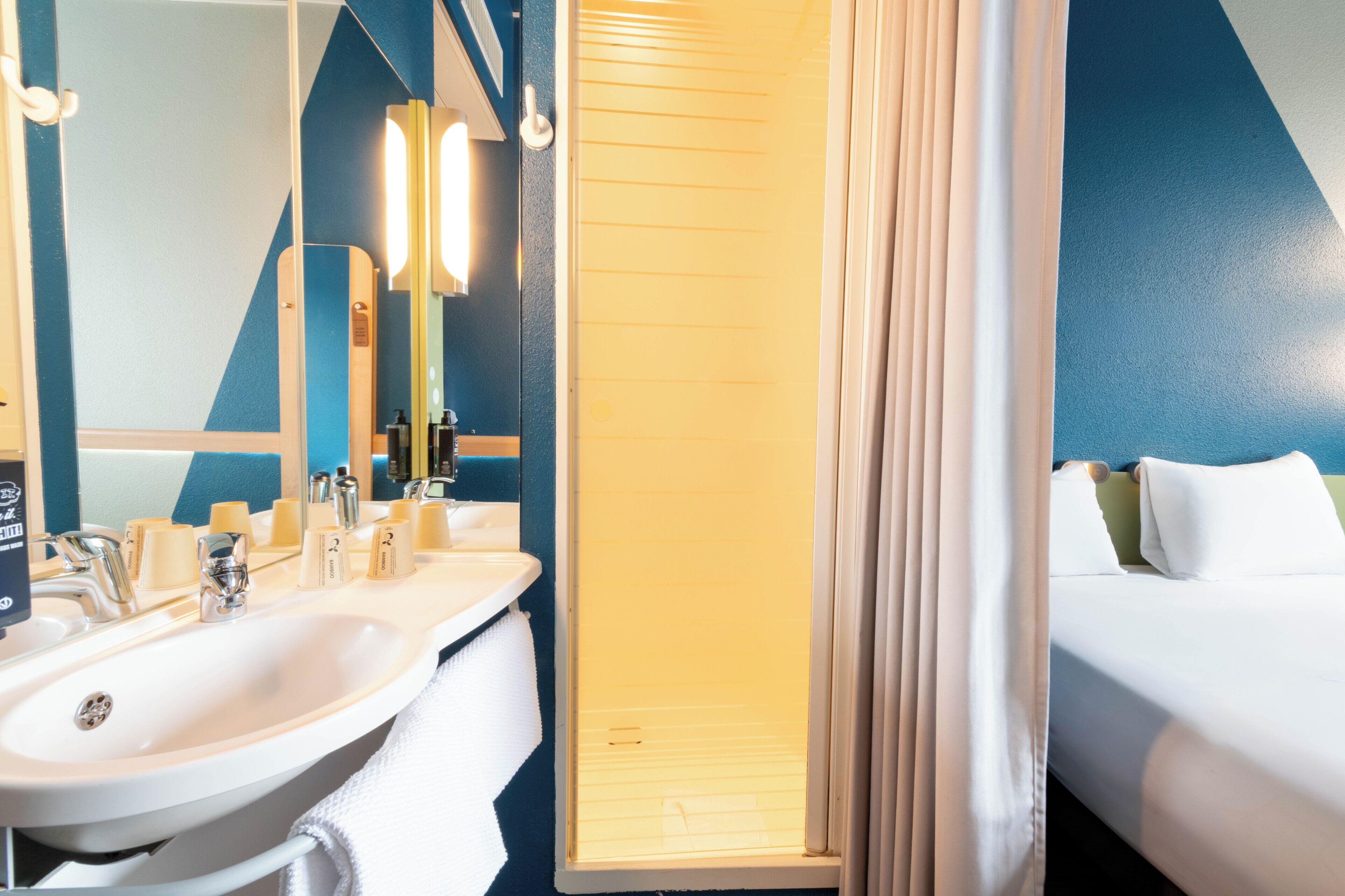 A hotel bathroom with a sink, mirror, and shower area.