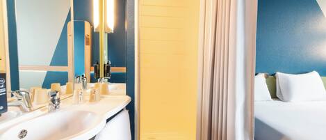 A hotel bathroom with a sink, mirror, and shower area.