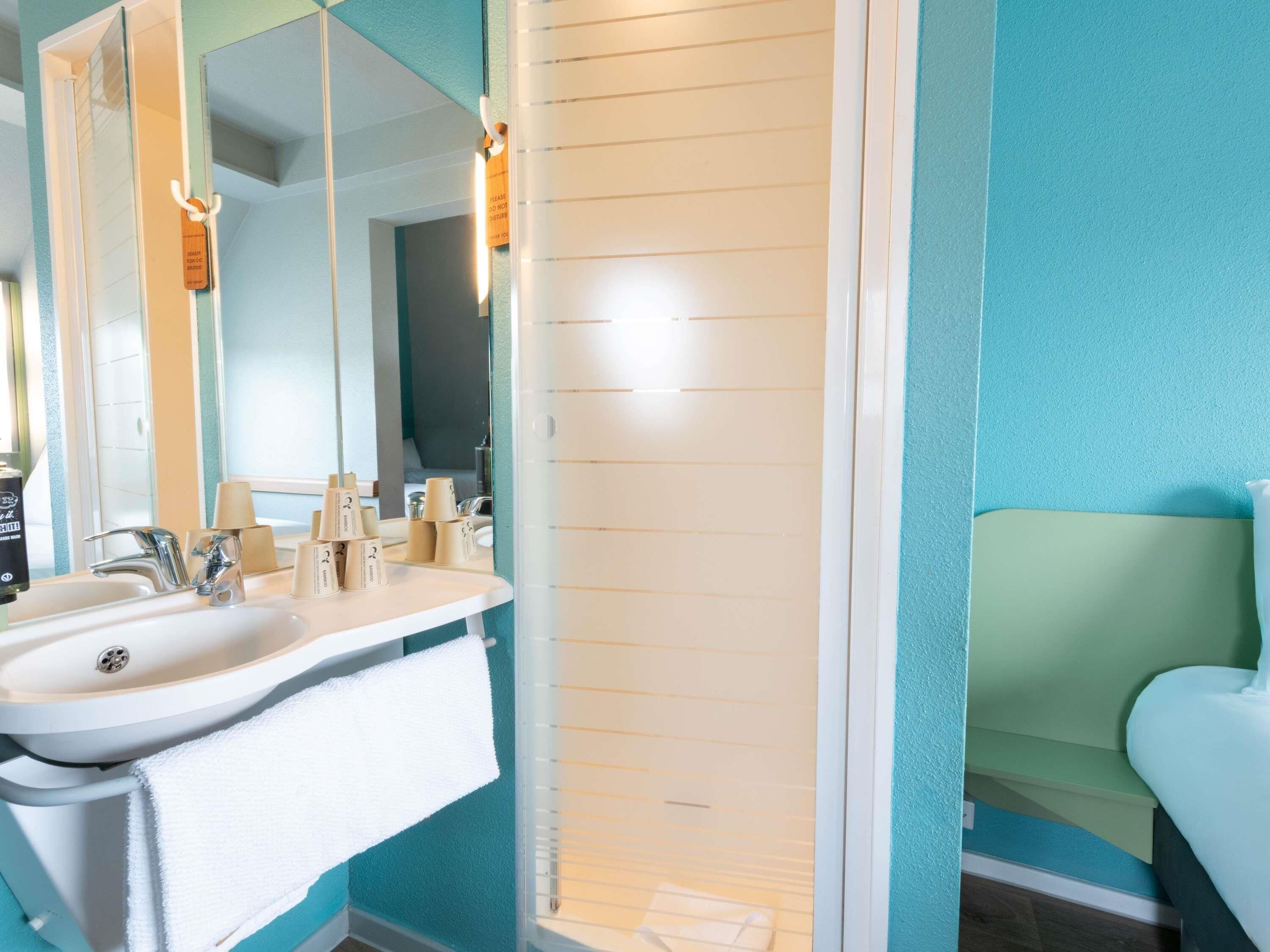 Un baño con un lavamanos blanco, dos espejos, un perchero y una ducha con puerta blanca.