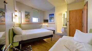 A hotel room with two single beds, a wooden floor, a shower area, and a television.