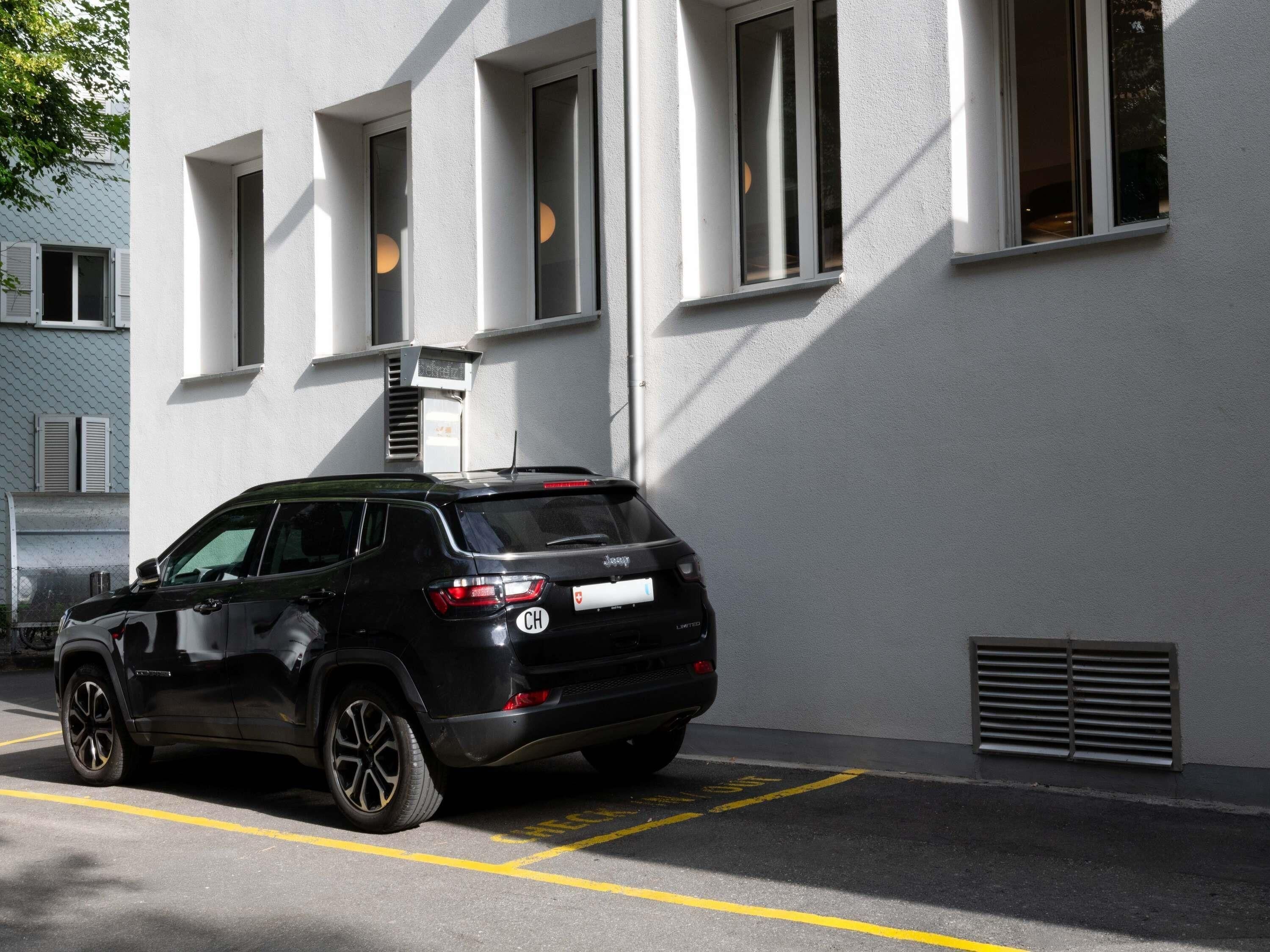 A black SUV parked in a parking space with a building featuring white walls and multiple windows in the background.