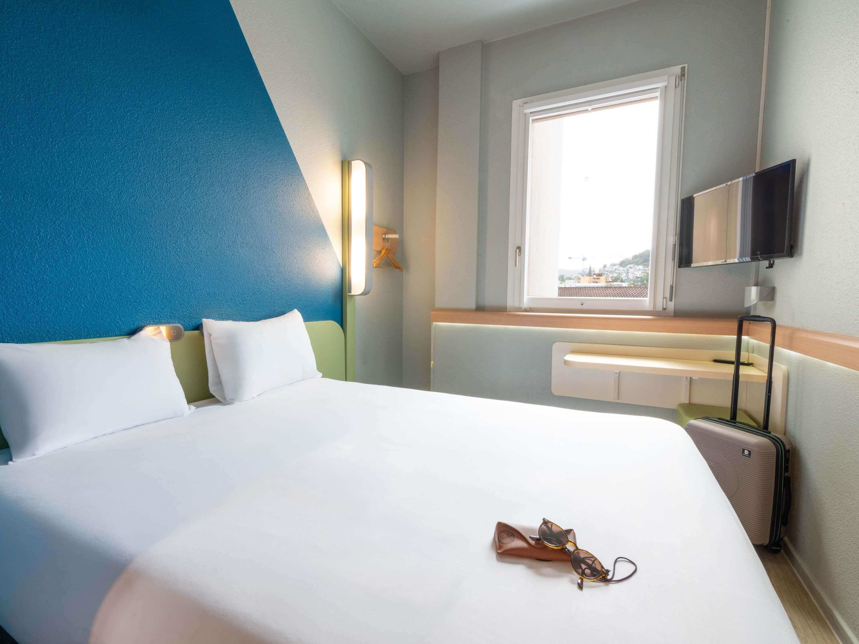 Une chambre d’hôtel avec un lit, une fenêtre, une télévision et une valise.