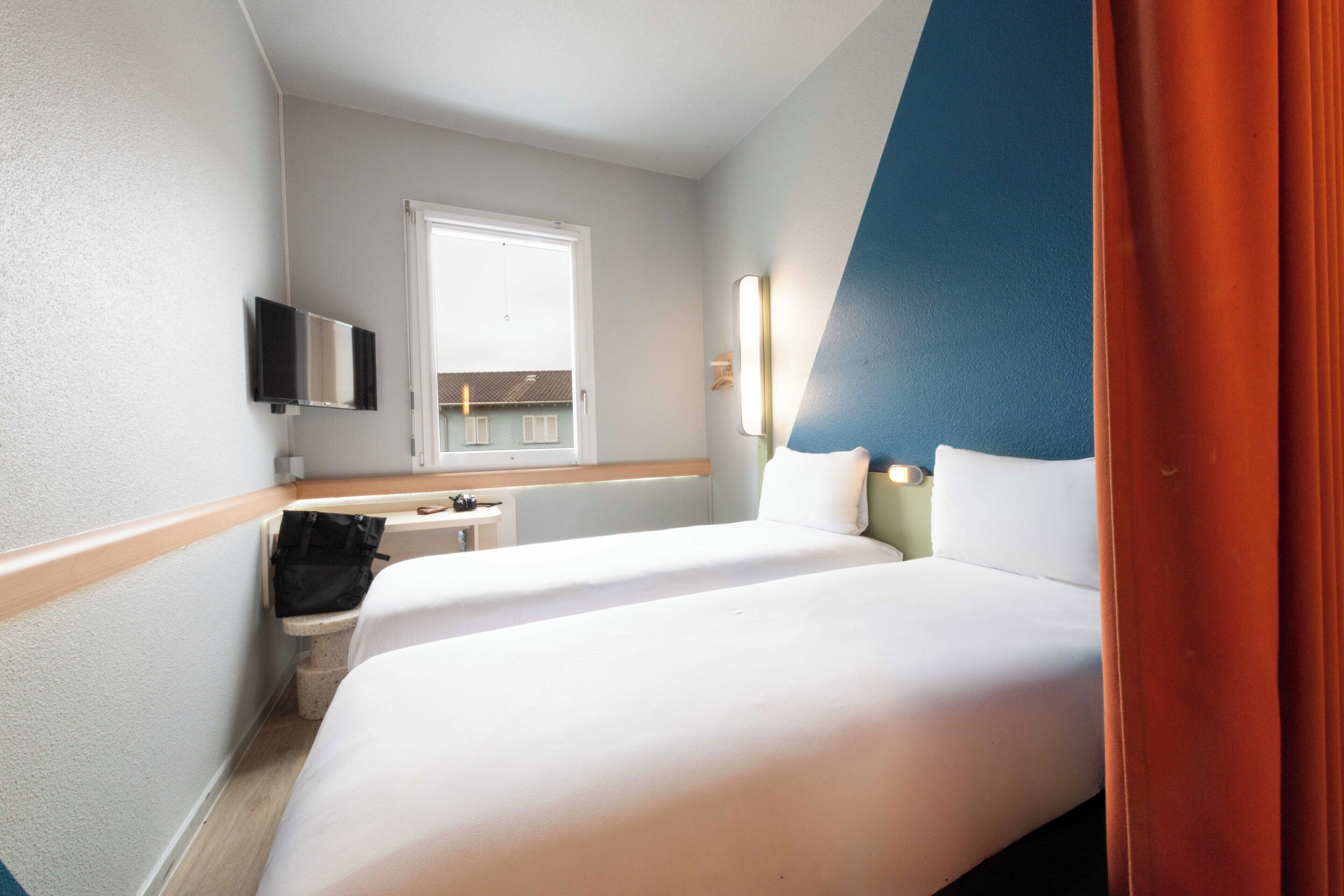 Une chambre d’hôtel avec un lit, un bureau, une chaise, une télévision et une fenêtre.