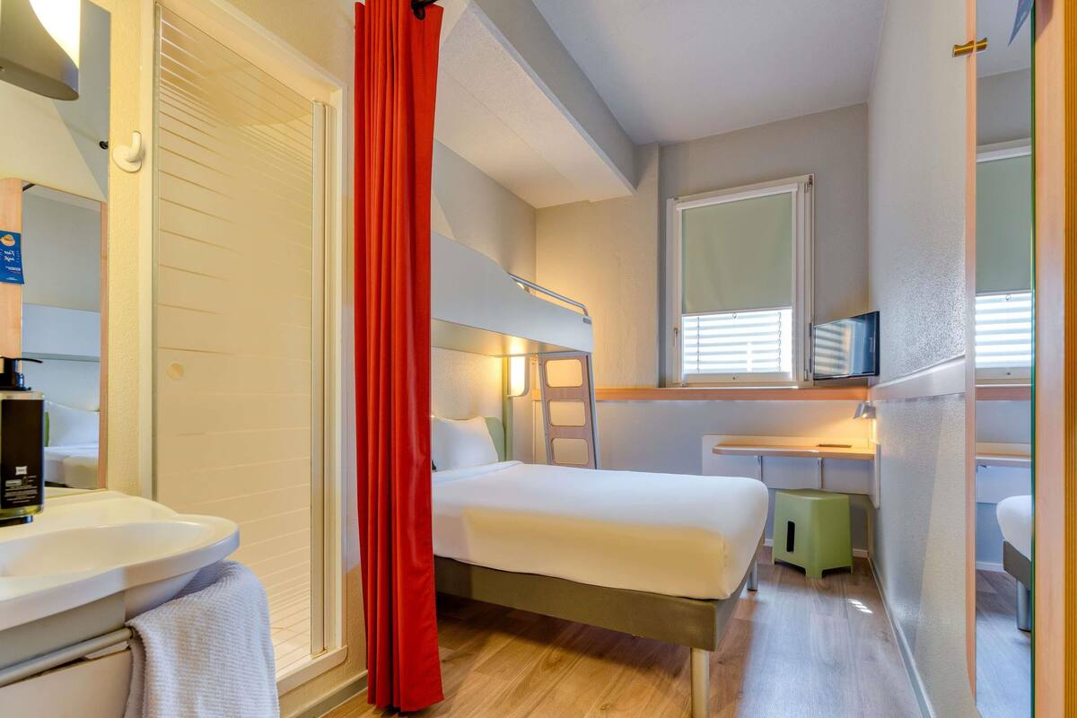 Ein kleines Hotelzimmer mit Bett, Nachttisch und einem Schreibtisch mit Stuhl.