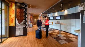 Un moderno vestíbulo de hotel con piso de madera, una recepción y una pared grande con varios carteles y una pantalla digital.