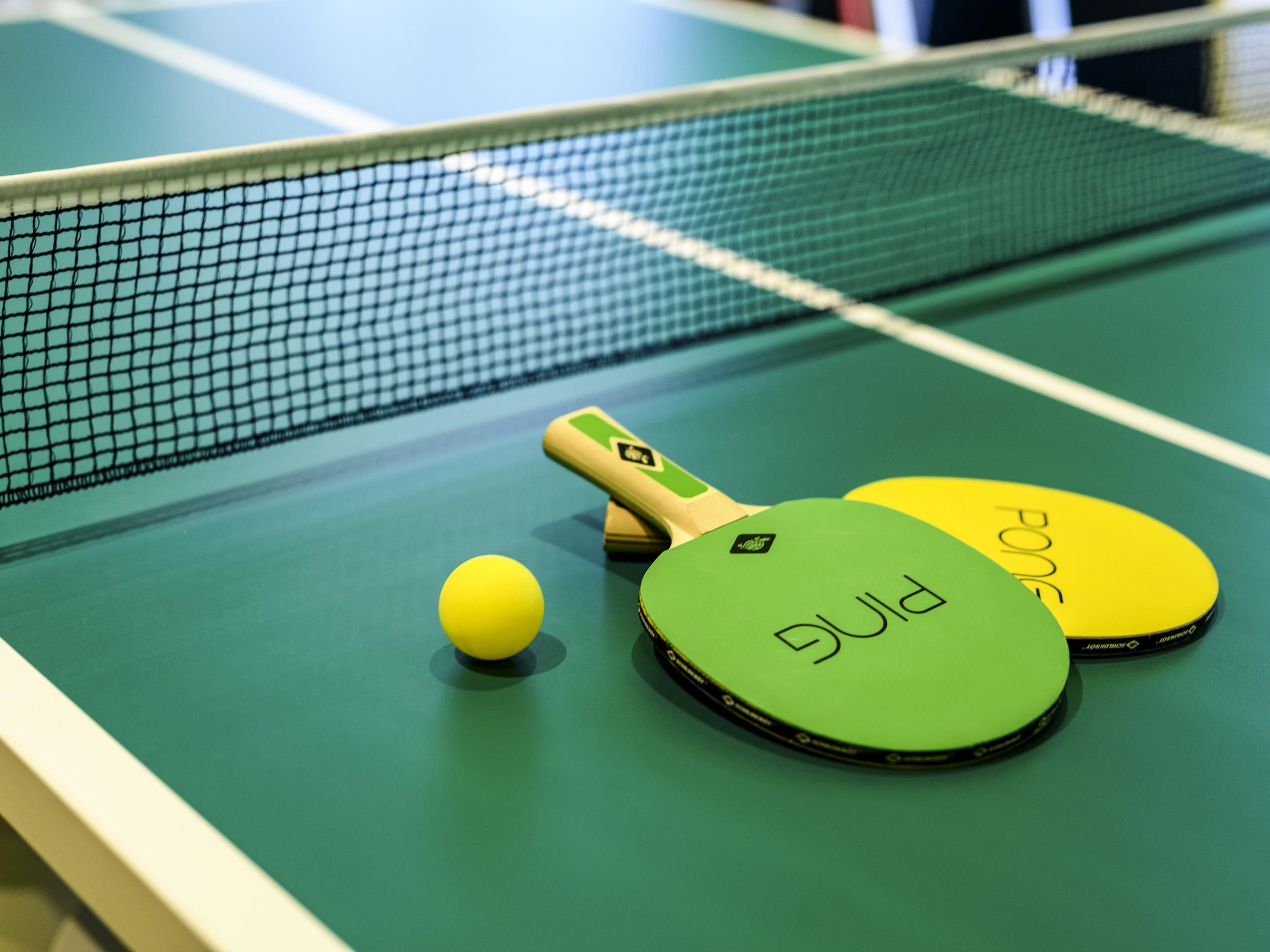 A table tennis table with a net, two paddles, and a ball.
