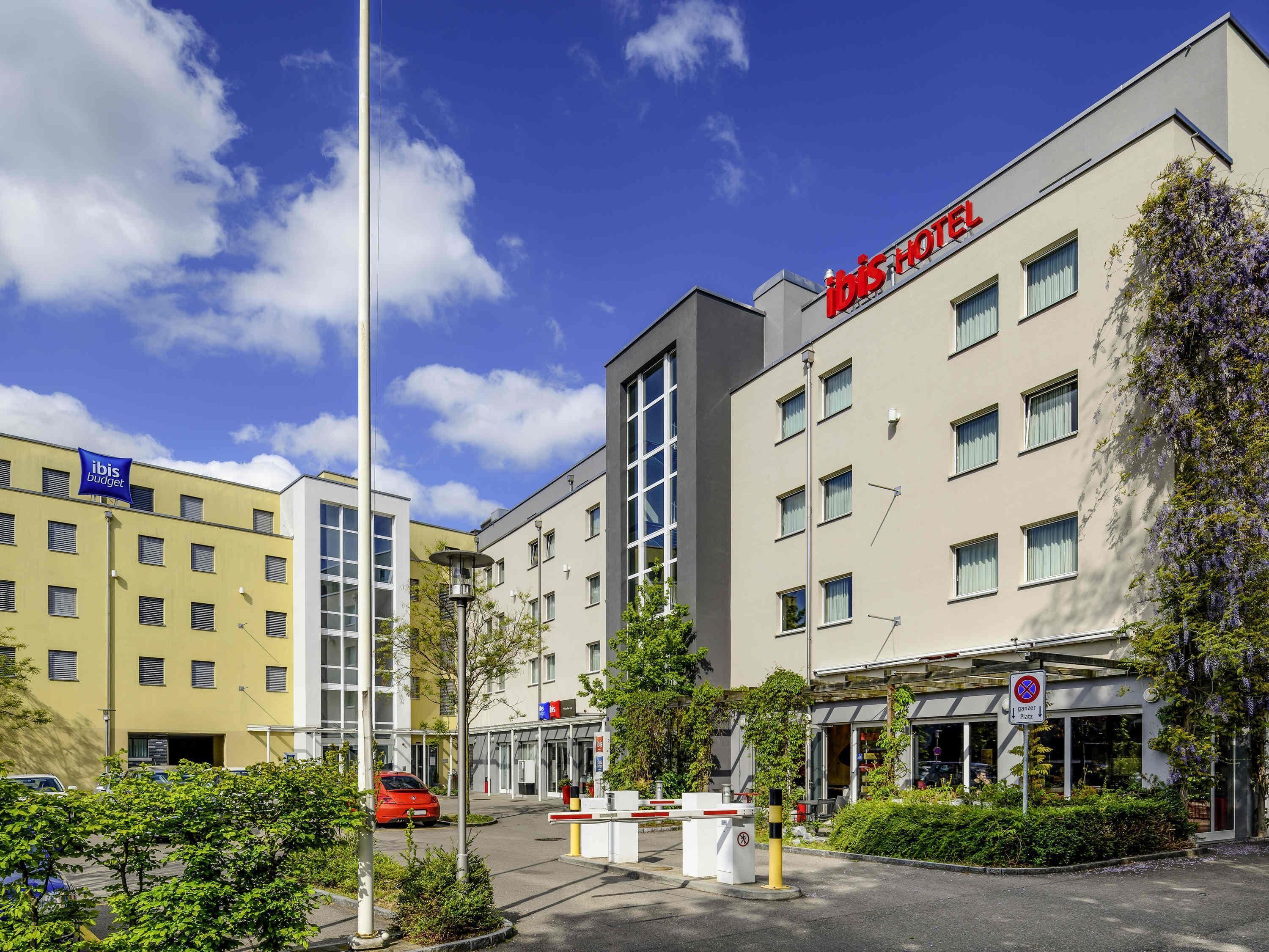 Ein Hotel mit modernem Design, gekennzeichnet durch eine auffällige rote Signage, zahlreiche Fenster und einen Eingangsbereich mit Tor.