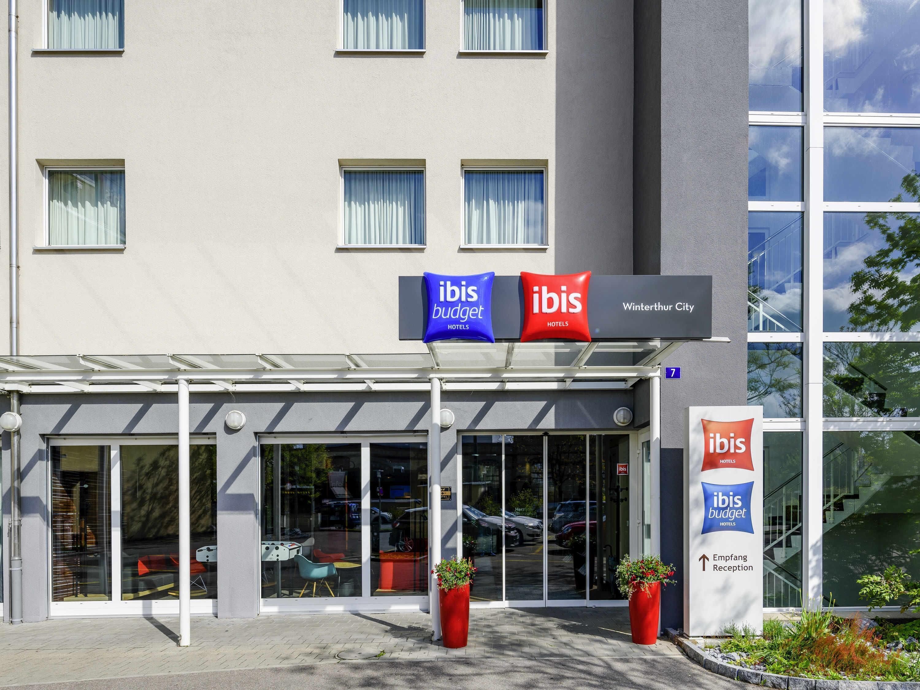 Ein Hotel mit Glastüren, einer überdachten Eingangspforte und Kübelpflanzen.