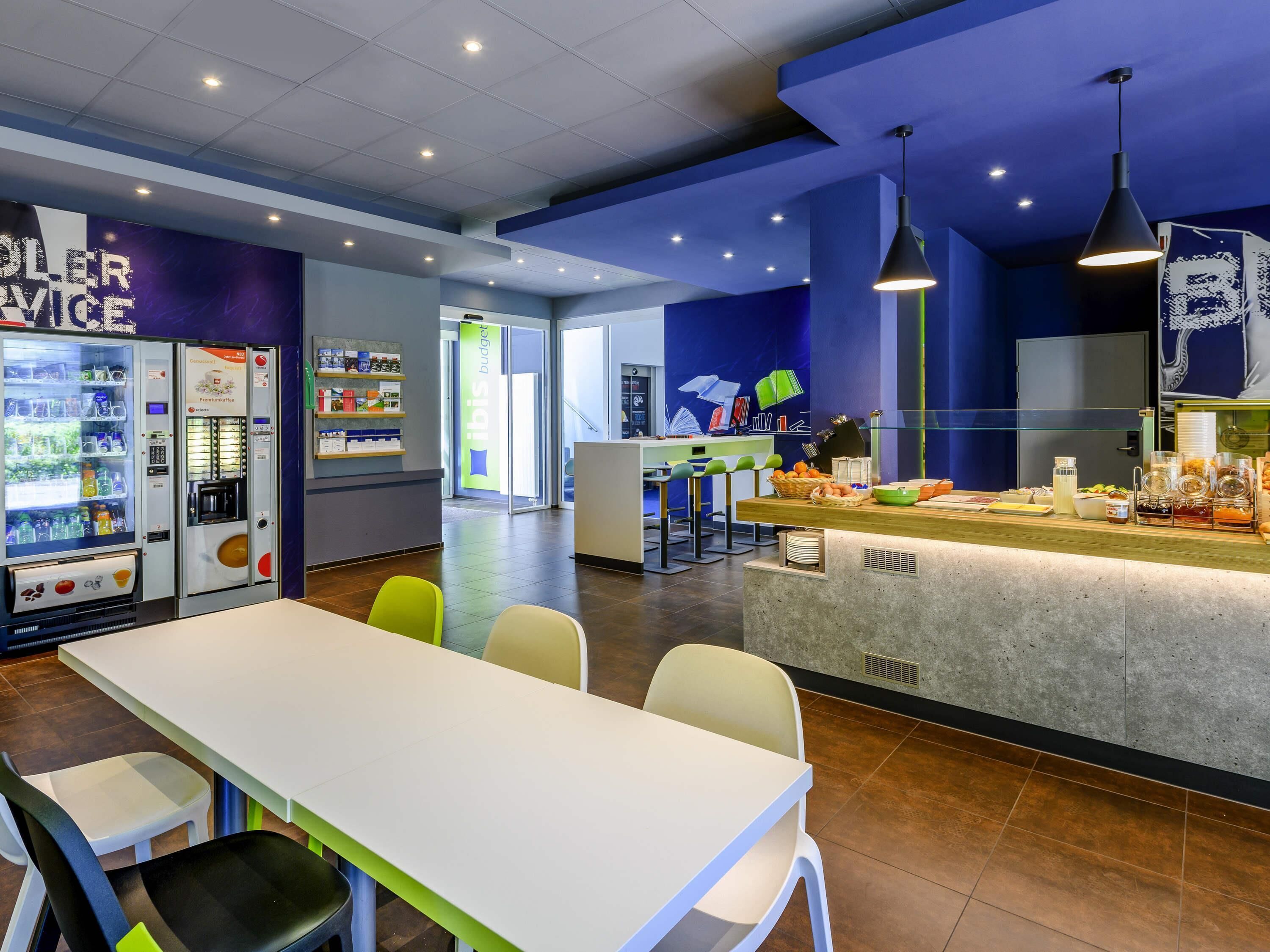 Un café moderne doté d’un espace salon, d’un comptoir où l’on sert des plats et des boissons, et de distributeurs automatiques.