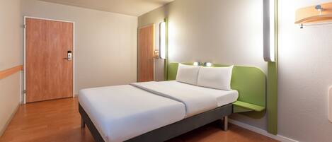 Habitación de hotel moderna con una cama individual, una puerta de madera y una pared de acento verde.