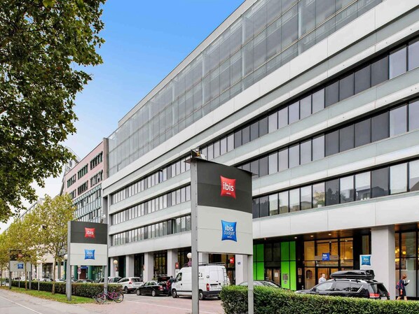 A modern hotel with a glass facade, multiple entry points, and clear signage for 'ibis budget' and 'ibis luxury' hotels.