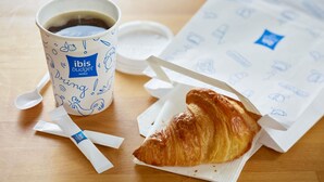 A cup of coffee, a croissant, and a napkin on a wooden table. - ibis budget Wien Messe (Vienna)