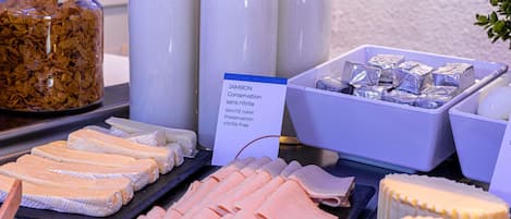 Un bufé con diversos alimentos, entre ellos jamón blanco, queso y cereales.