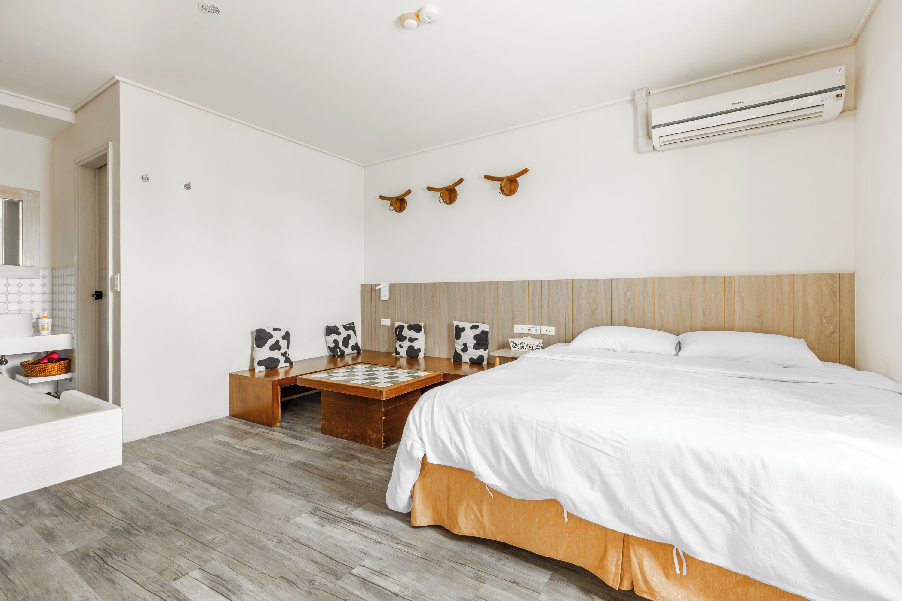 Un dormitorio moderno con cabecera de madera, una cama grande, una mesita de noche de madera, una pequeña mesa con un tablero de ajedrez y un aire acondicionado de pared.
