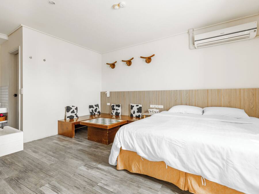 Un dormitorio moderno con cabecera de madera, una cama grande, una mesita de noche de madera, una pequeña mesa con un tablero de ajedrez y un aire acondicionado de pared.