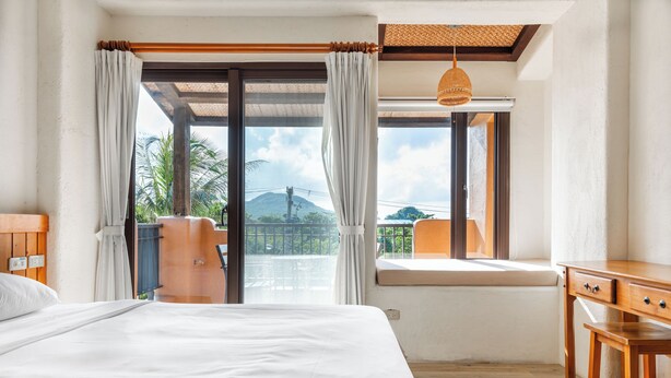 A bedroom with a large bed, a wooden desk, and a window with a view of palm trees and a mountain. - Kenting Fairyland & Farm Guest House (Hengchun)