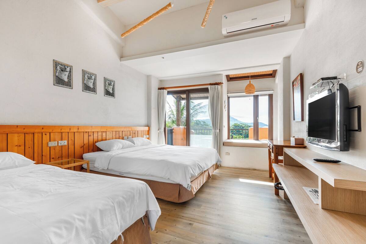 Ein Hotelzimmer mit zwei Betten, einem Fernseher, einer hölzernen Bank und einem Balkon mit Blick.