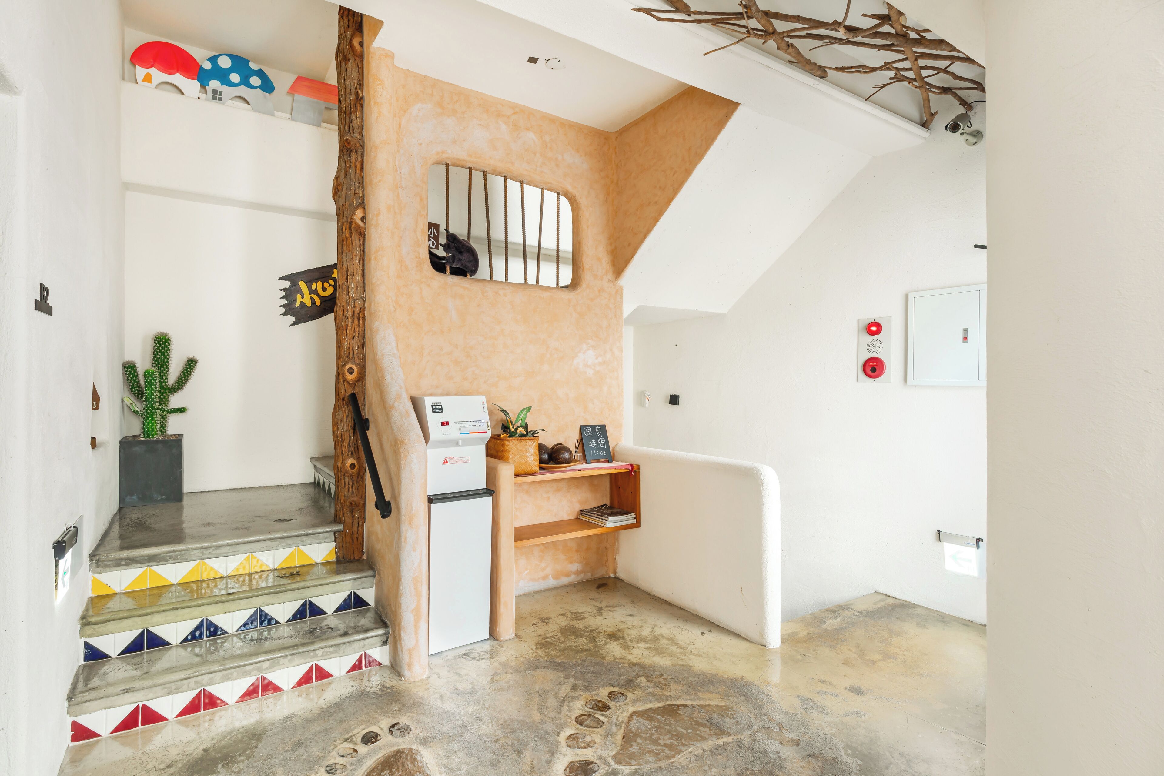 A staircase with colorful tiles, a small refrigerator, and a shelf with plants and a chalkboard.