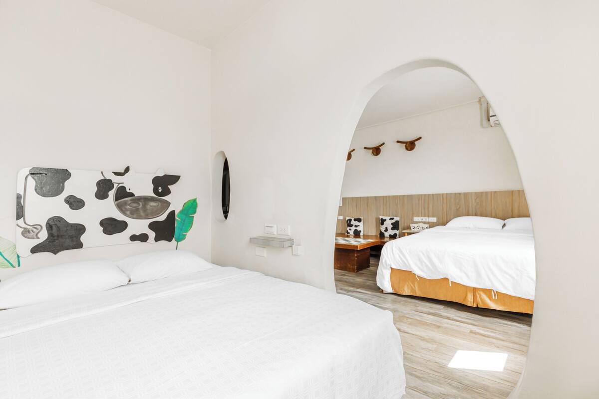 Ein Hotelzimmer mit einem großen Bett, einem Schreibtisch und Blick durch einen Bogen in ein weiteres Zimmer.