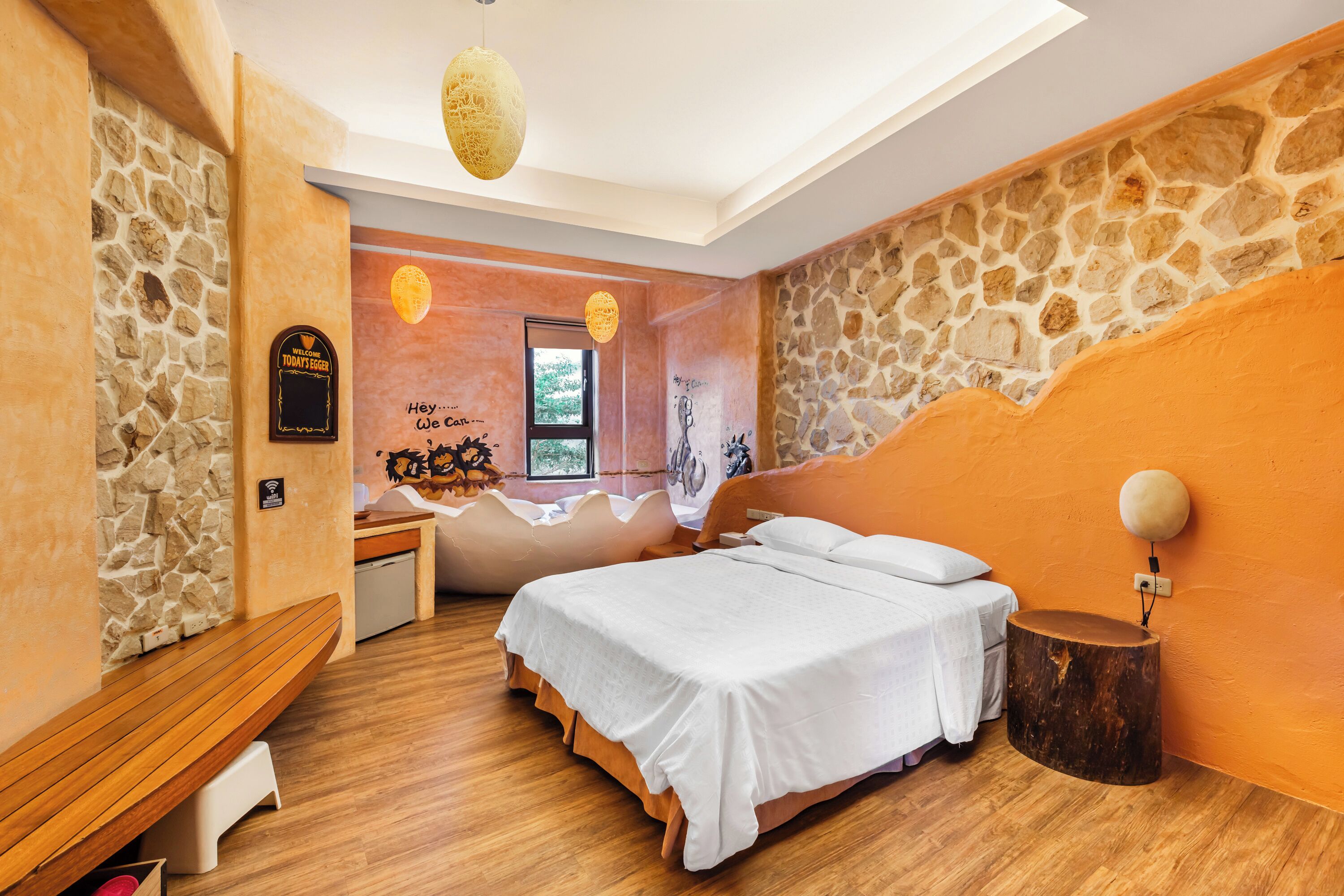 A bedroom with a stone wall, a wooden bench, a bed with white bedding, and a round wooden table.