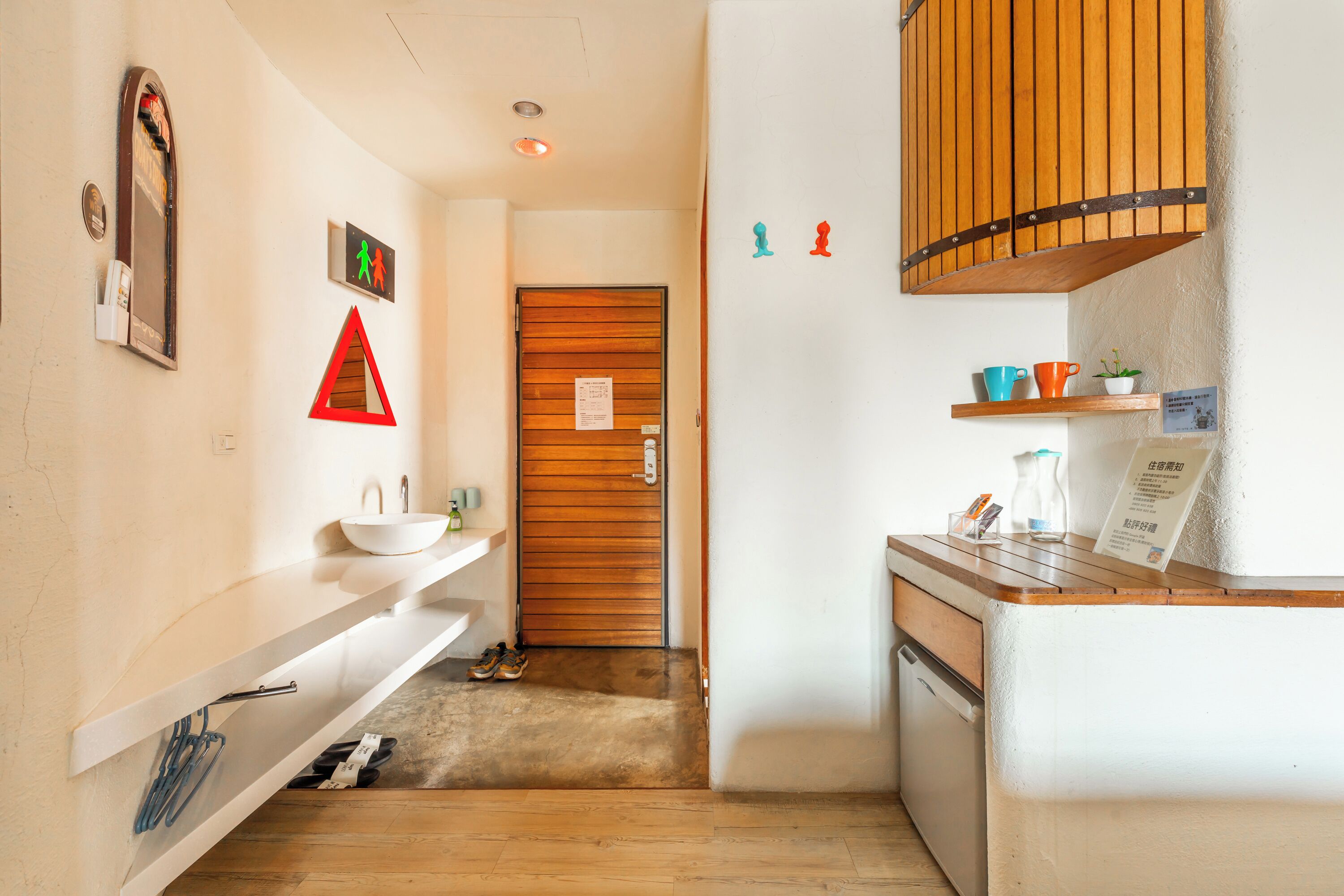A hallway with a wooden door, a white sink, and a small shelf with cups and a plant.