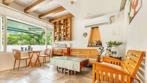 A spacious living area with a wooden bench, a glass-top table, and a bookshelf filled with books and decorative items. - Kenting Fairyland & Farm Guest House (Hengchun)